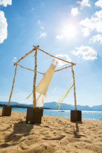 bride's dress hanging from ceremony arch on beach, sun flare, blowing unwind – South Lake Tahoe lakefront beach wedding nina photographer