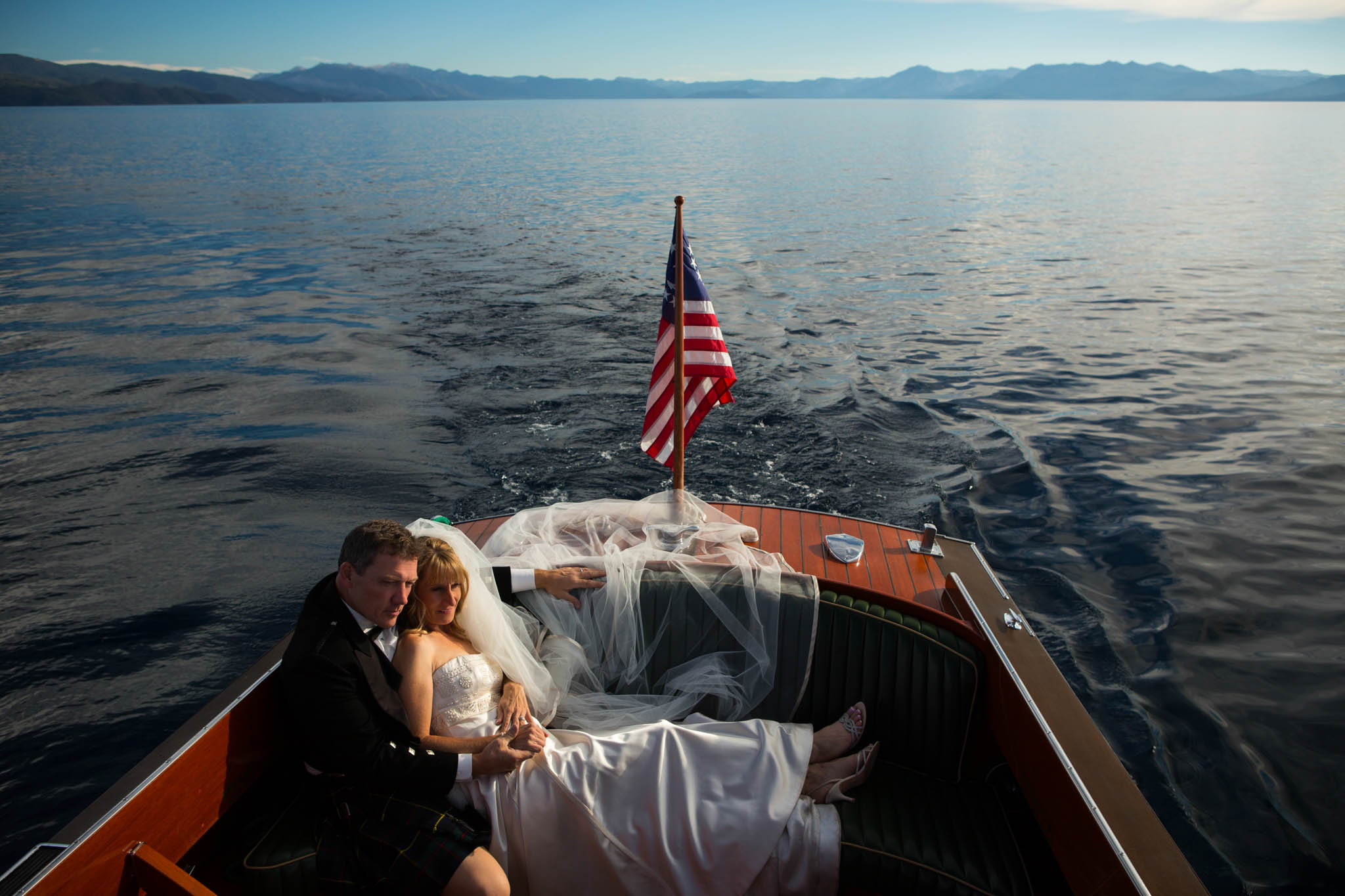 bride groom on wooden boat on lake flag mountains – Fairwinds Tahoe wedding photography