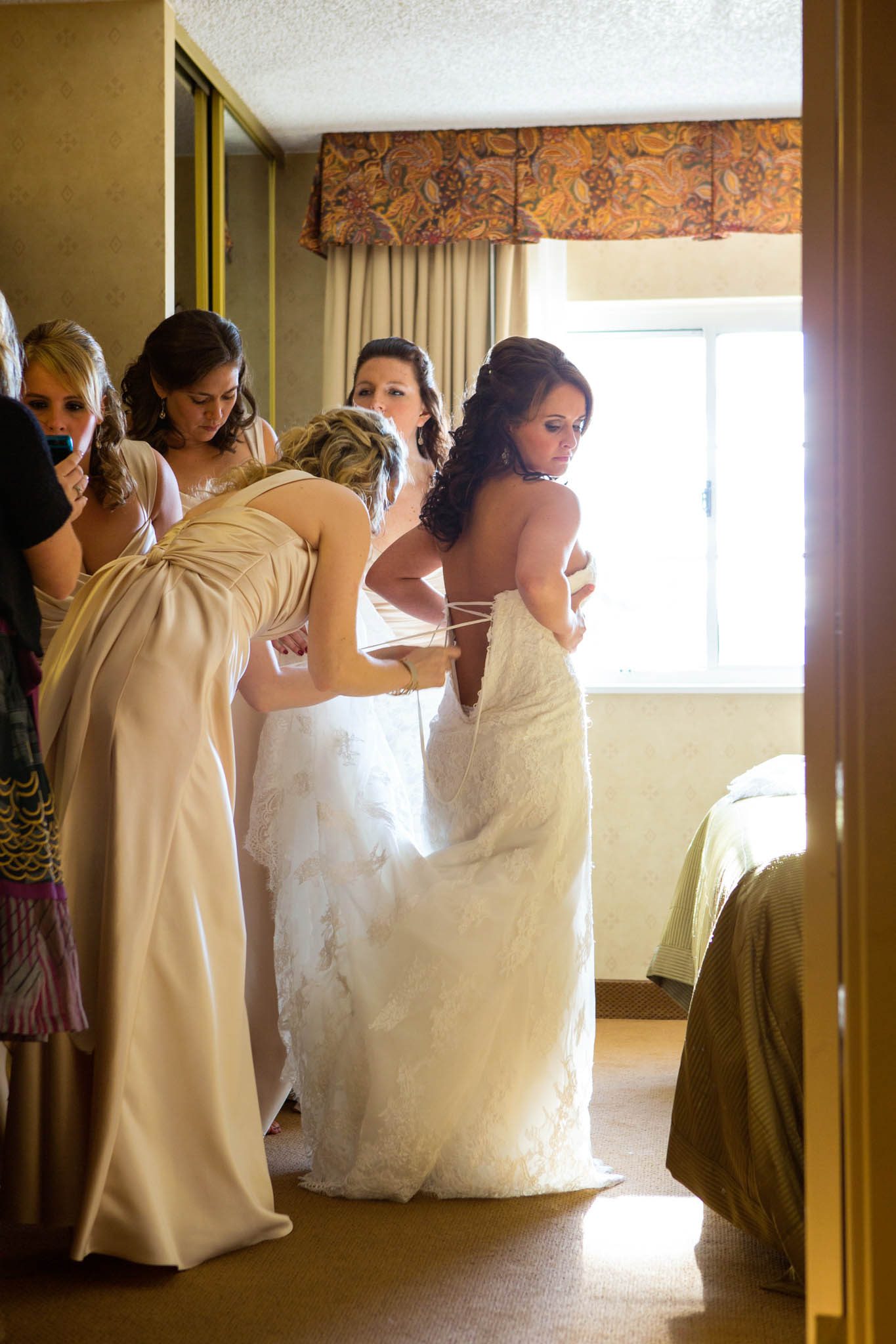 bride getting ready, putting on dress, bridesmaids lacing dress, champagne dresses, backlight