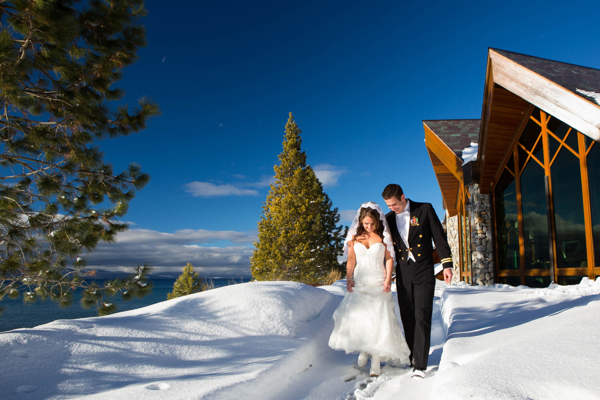 bride and groom walking through snow by Edgewood, blue sky