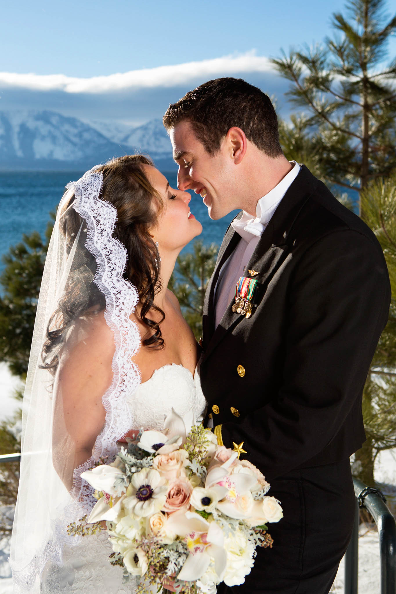 bride and groom kissing, smiling, lake view, snow, white bouquet, uniform