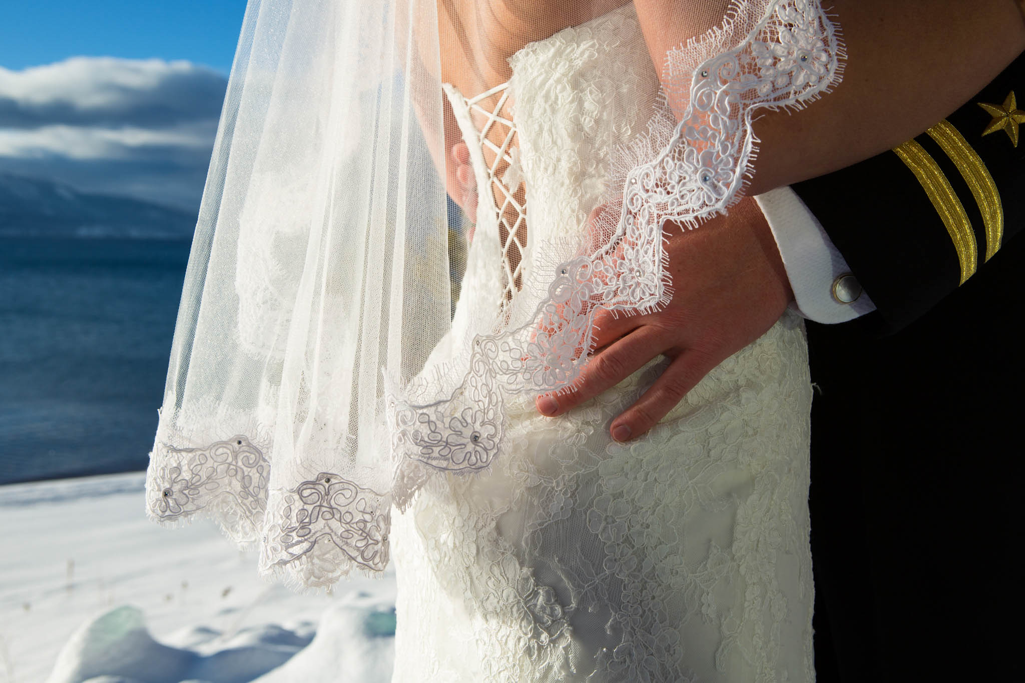 bride and groom close-up of dress, veil, hand, lace, lake, blue, snow